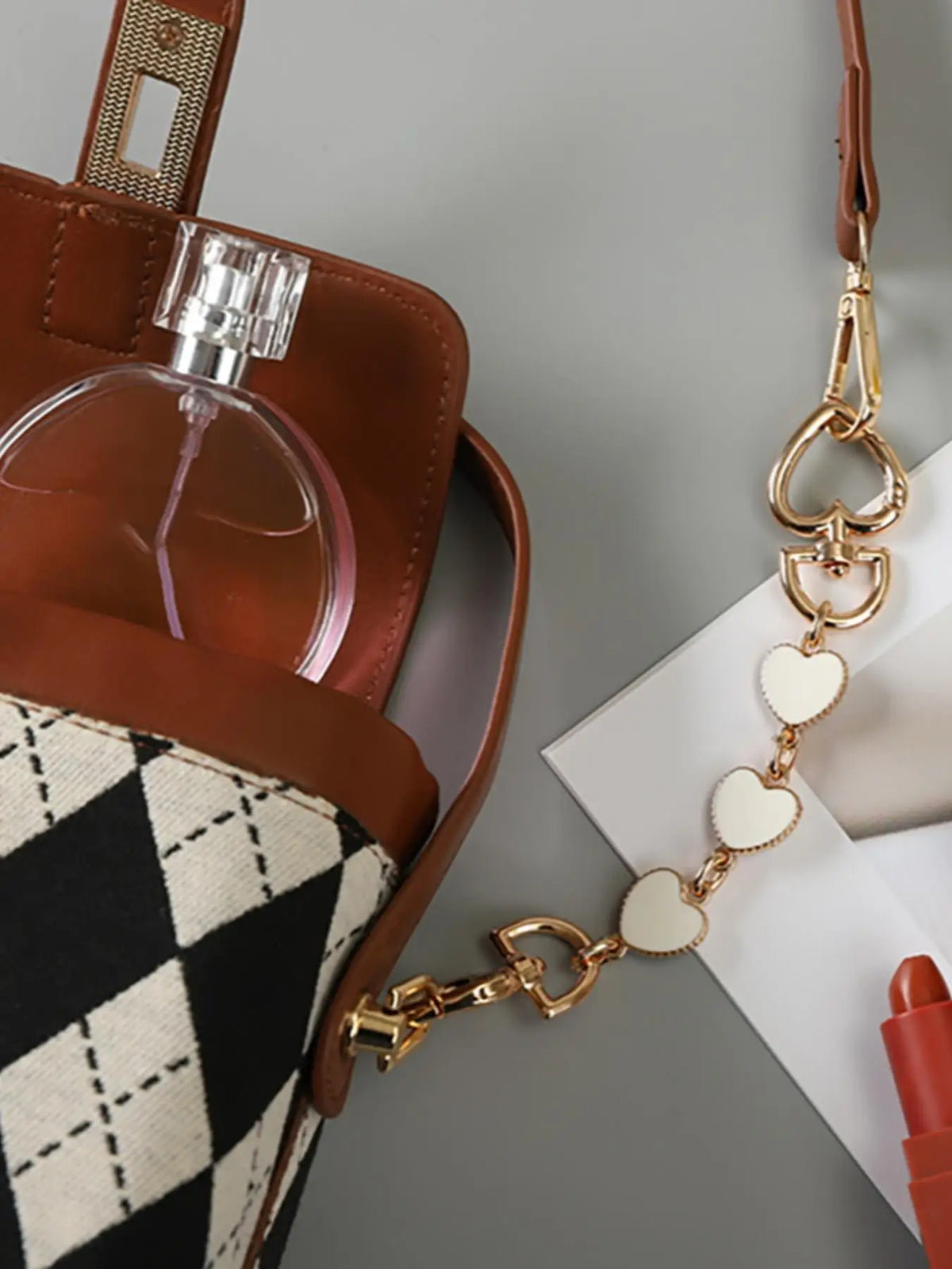 Un jeu d'extenseurs de chaîne pour porte-monnaie ajustable ton or, à côté d'un sac en cuir marron et d'une enveloppe blanche.