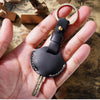 A hand holds a black leather key fob cover with a metal ring and key attached.