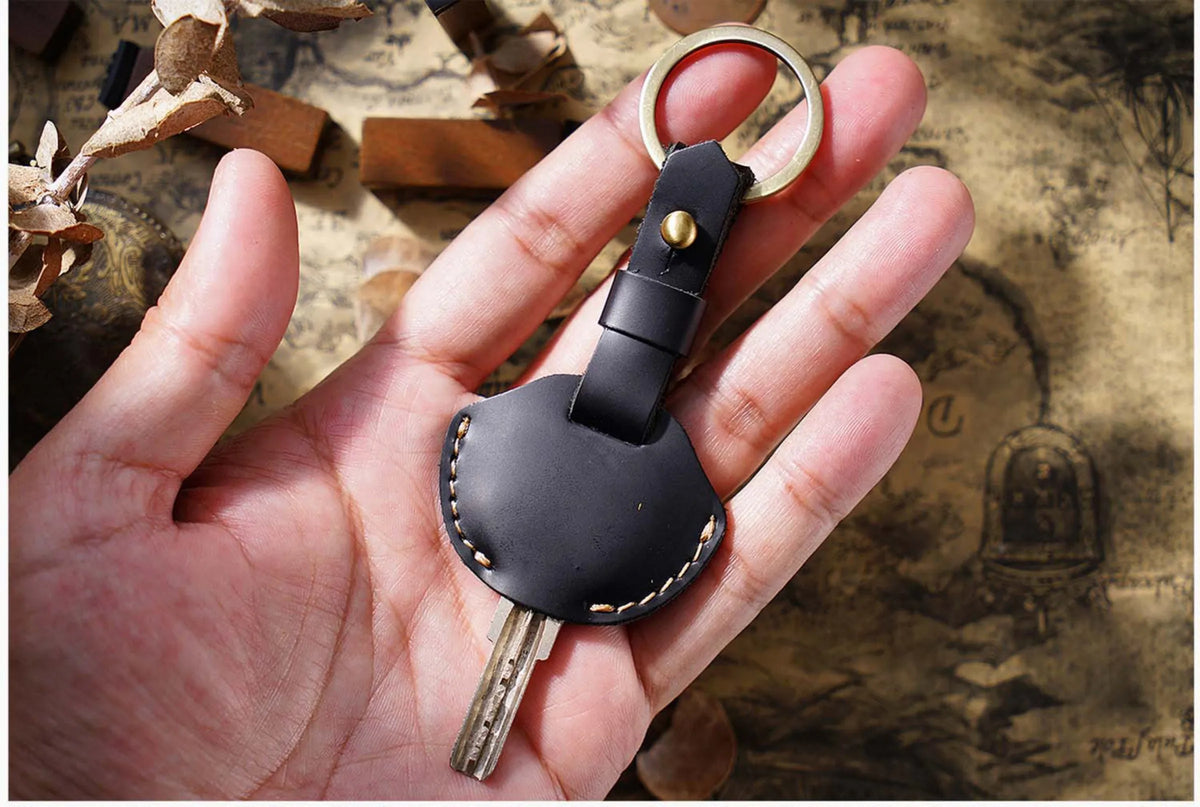 A hand holds a black leather key fob cover with a metal ring and key attached.