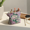 A purple floral canvas makeup bag filled with makeup brushes and cosmetic tools on a white surface.