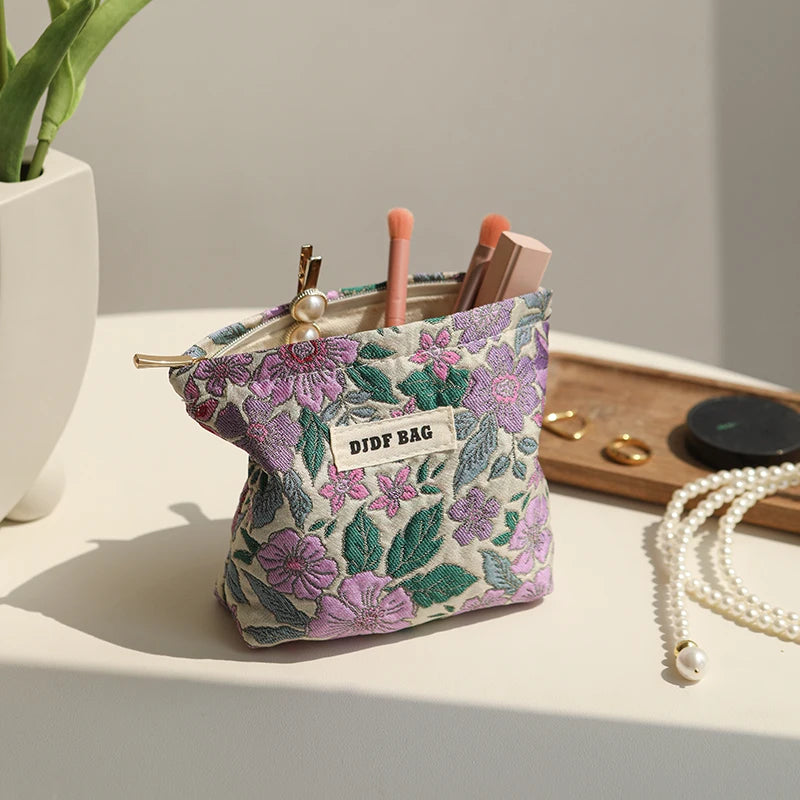 A purple floral canvas makeup bag filled with makeup brushes and cosmetic tools on a white surface.