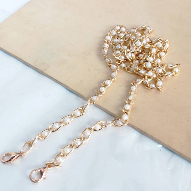 A delicate gold chain strap made of small white pearls resting on a beige rectangular surface.