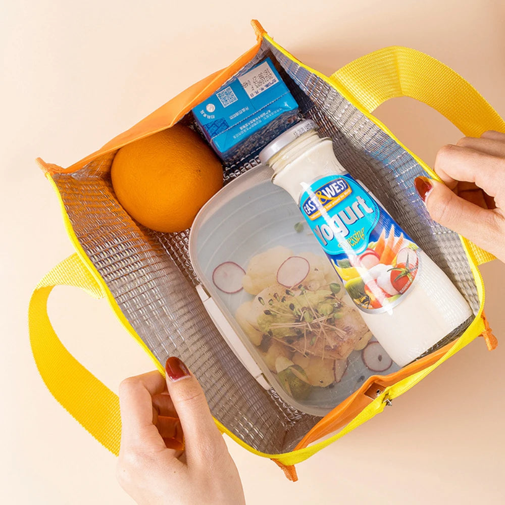 A hand holds an orange and yellow insulated lunch bag containing a juice bottle and a small box.