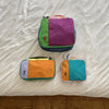 A set of three waterproof travel toiletry bags in green, purple, and orange resting on a white sheet.