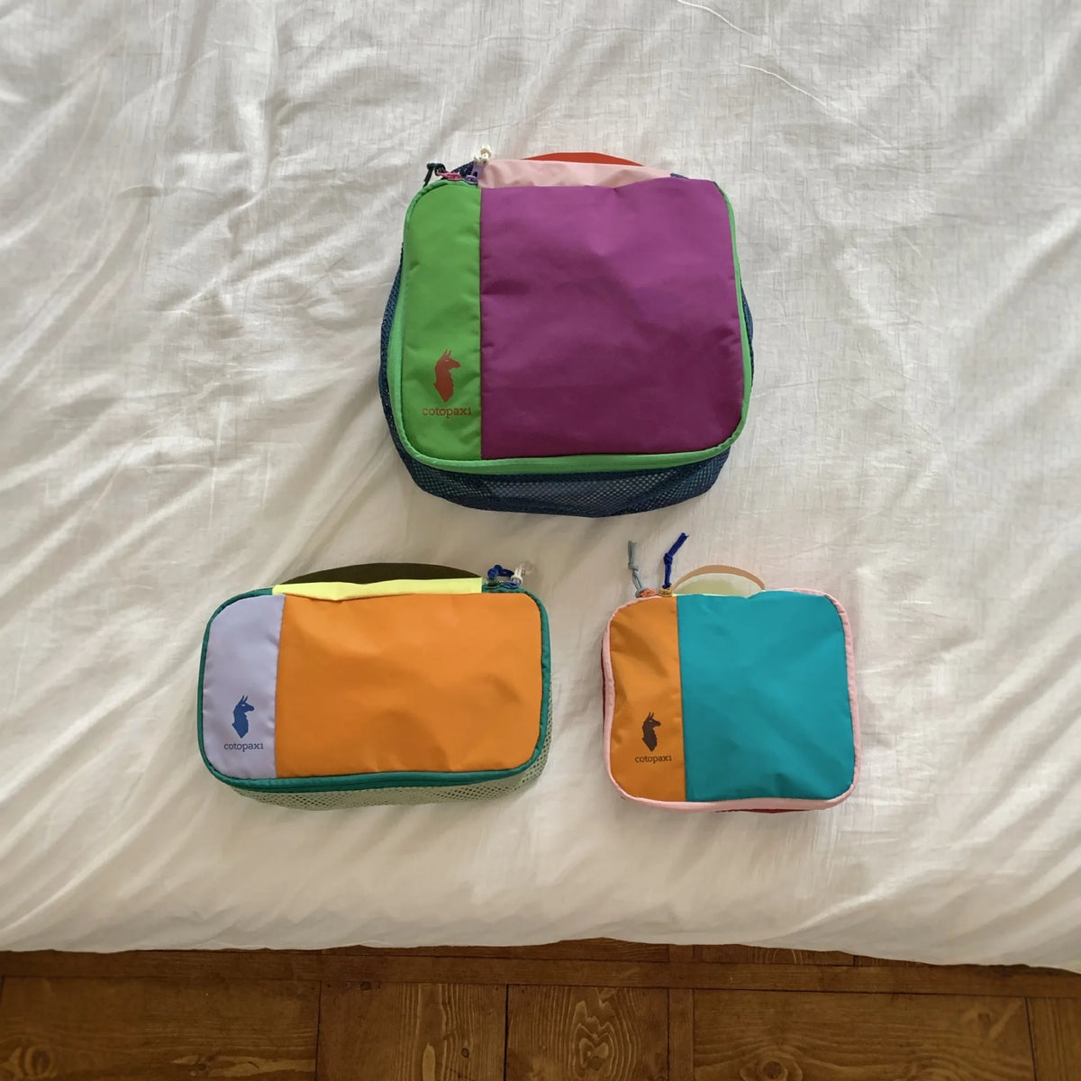 A set of three waterproof travel toiletry bags in green, purple, and orange resting on a white sheet.