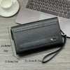 A black crocodile pattern clutch bag lying on a wooden desk next to a silver laptop and a white cup.