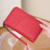 A red leather RFID blocking travel wallet is held by a hand above a clear acrylic stand.