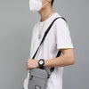 Eine Person mit schwarzer Kappe und Gesichtsmaske hält eine graue kompakte Crossbodytasche.