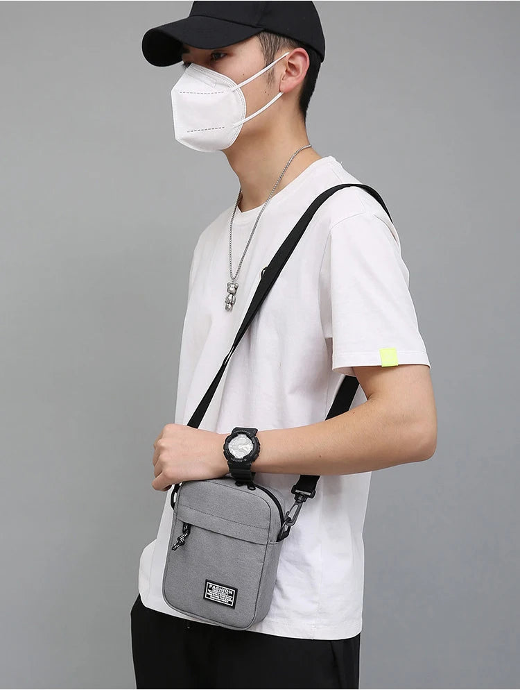 Eine Person mit schwarzer Kappe und Gesichtsmaske hält eine graue kompakte Crossbodytasche.