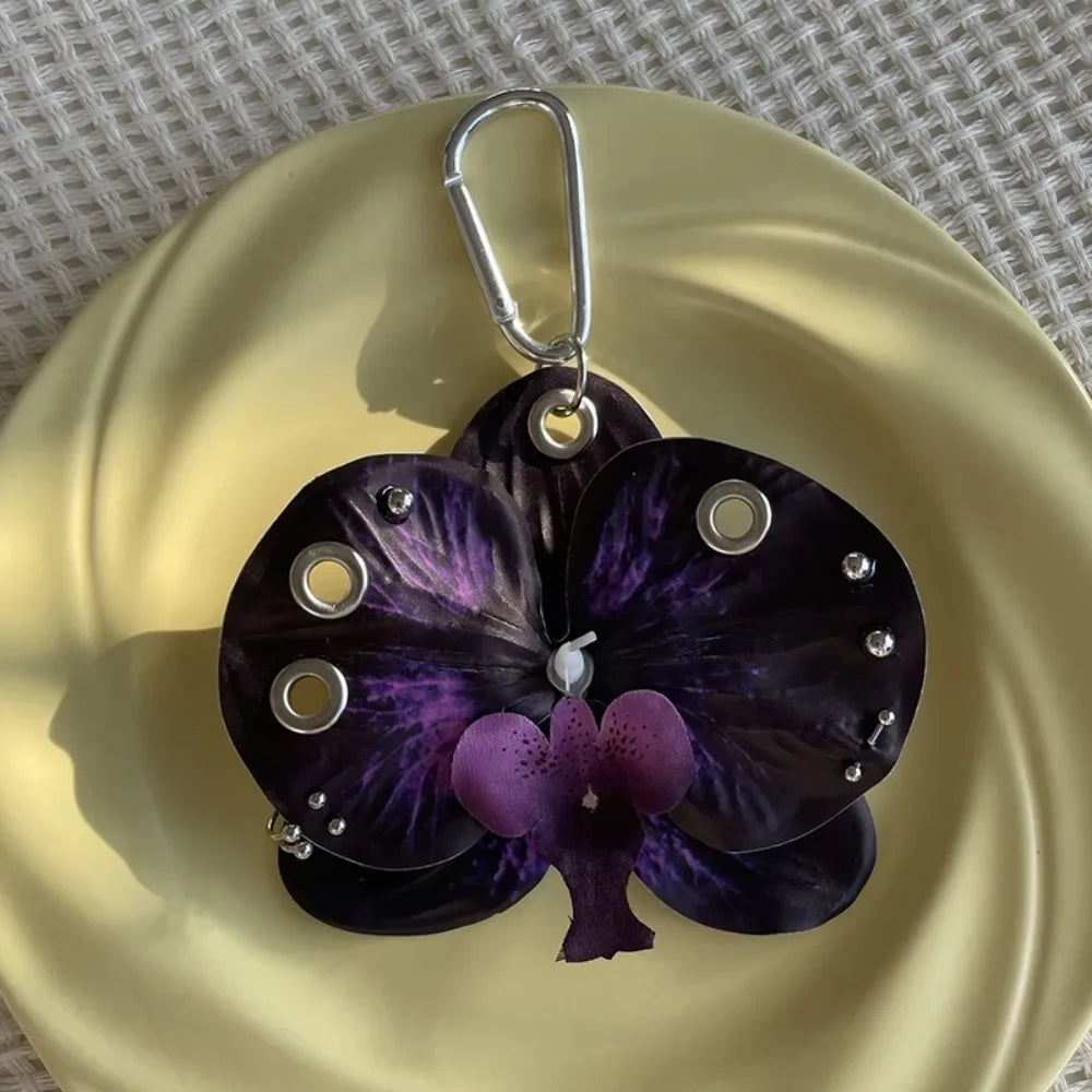 A dark purple orchid flower keychain with silver hardware resting on a gold plate.