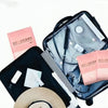 A black suitcase contains a set of pink disposable bathtub liners and a straw hat.
