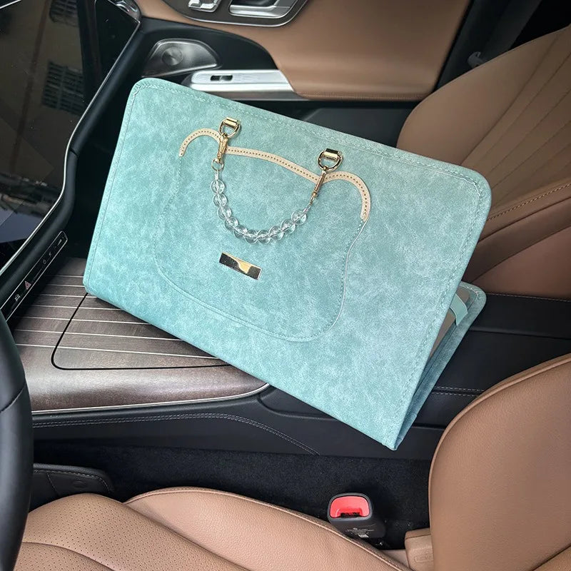A teal laptop sleeve with a gold chain strap is placed on the center console of a car interior.