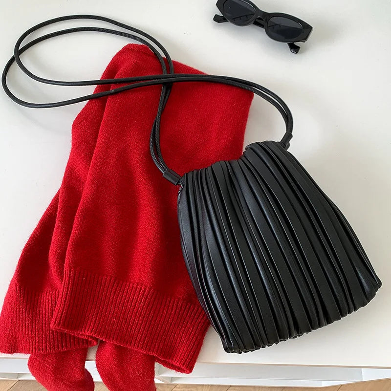 A red knitted sweater and a black PU leather pleated crossbody bag are displayed on a white surface.