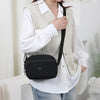 A woman wearing a beige vest over a white shirt and black nylon crossbody bag.