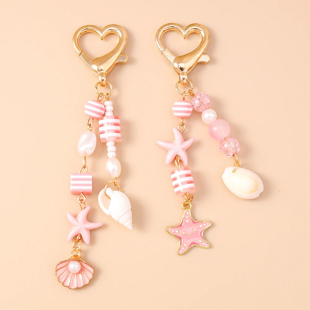 Gold heart-shaped keychain featuring a starfish and pearl accents with pink and white striped beads.