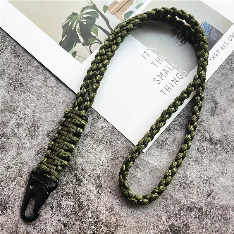 A hand-woven green nylon lanyard with a metal hook displayed on a gray textured surface.