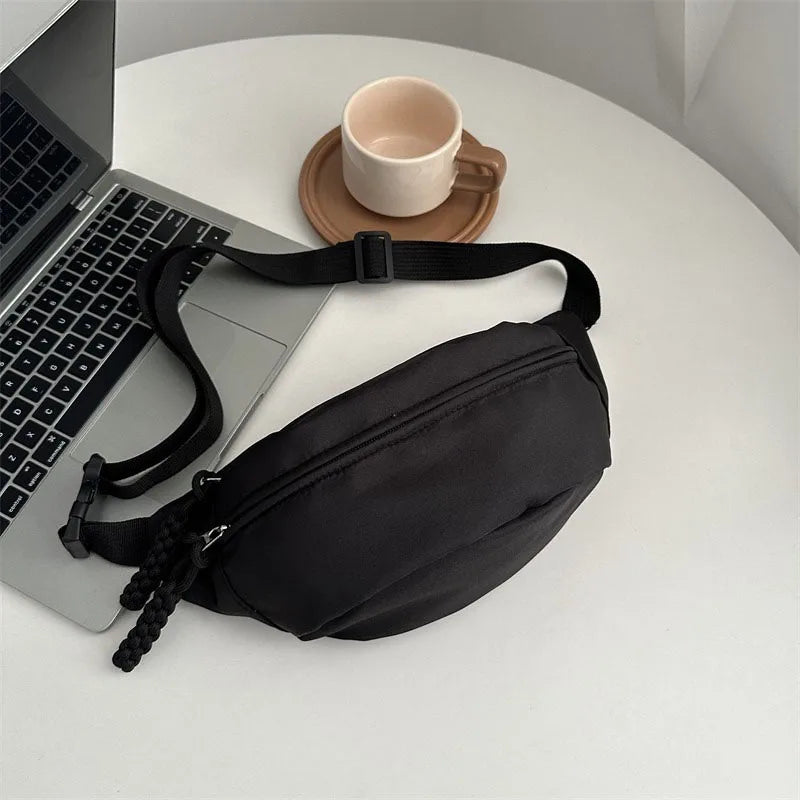 A black anti-theft waist pack is displayed next to a laptop and a ceramic mug on a white surface.
