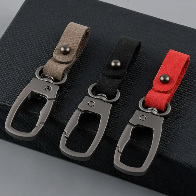 Three leather keyring keychains in shades of brown, black, and red displayed on a dark surface.