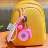 A yellow backpack with a pink fitness keychain featuring a dumbbell and kettlebell charm.
