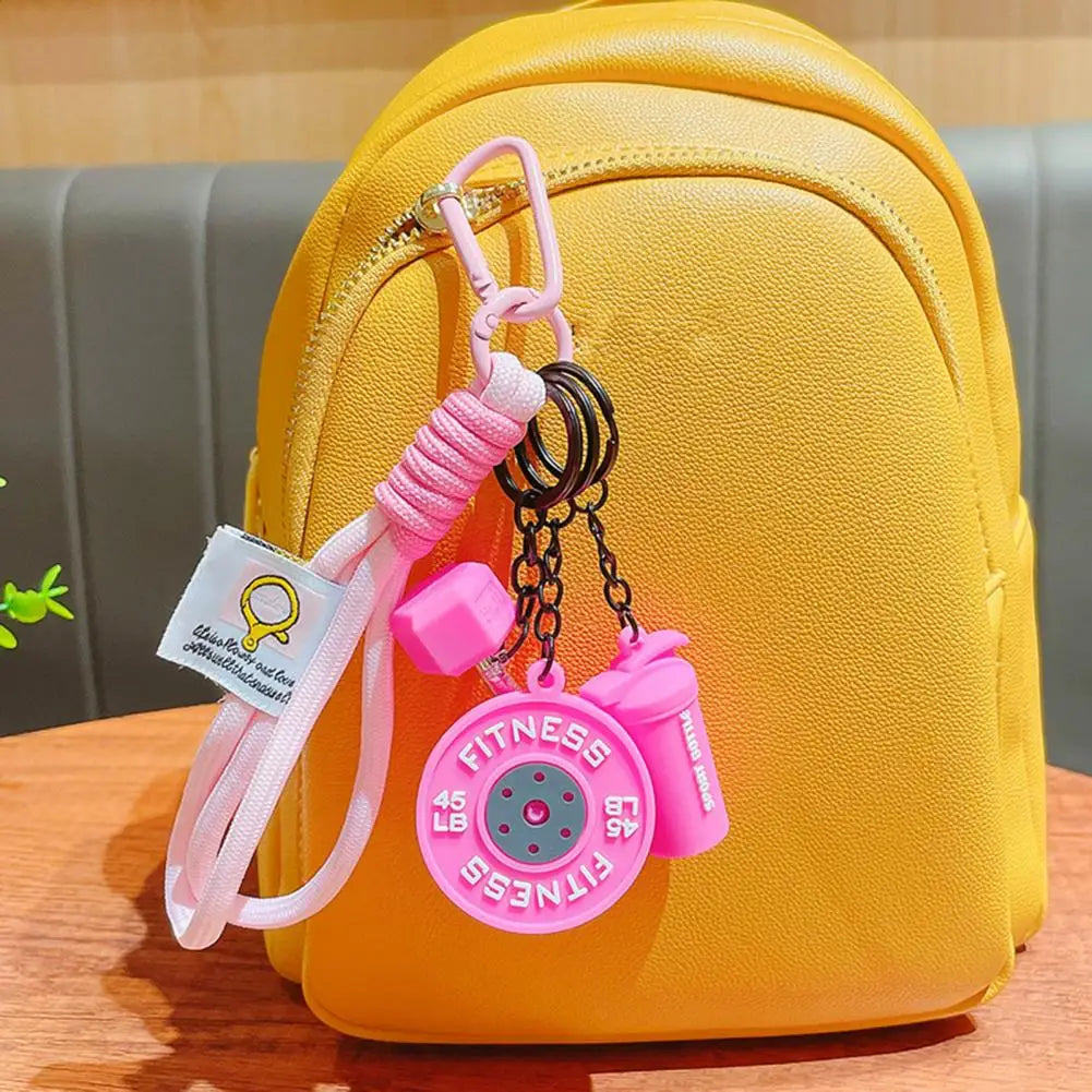 A yellow backpack with a pink fitness keychain featuring a dumbbell and kettlebell charm.