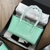 A light mint green crocodile print leather handbag is displayed in a black box with white tissue paper.