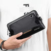 A black leather everyday crossbody bag with a gold accent is held by a hand against a white t-shirt.