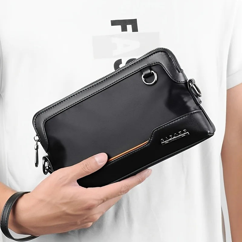 A black leather everyday crossbody bag with a gold accent is held by a hand against a white t-shirt.