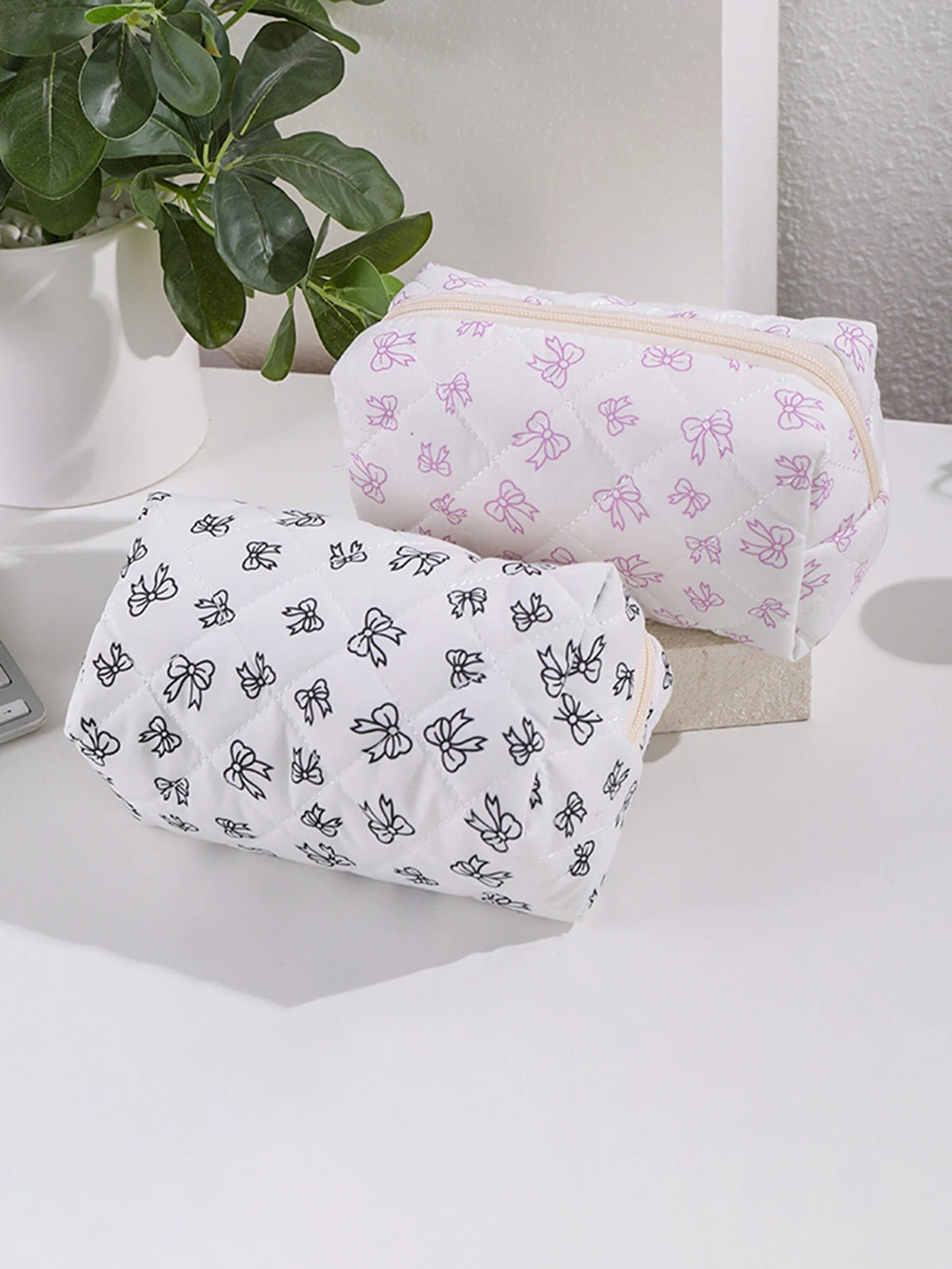 Dos bolsitas cosméticas con estampados de lazo en blanco y lila claro exhibidas sobre una superficie blanca.