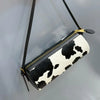 A black and white cow print cylinder shoulder bag hanging from a black strap.