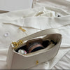A light beige elegant PU leather hobo shoulder bag with gold hardware resting on a white fabric background.