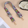 A colorful floral patterned nylon crossbody bag strap with a metal buckle is displayed next to a pearl necklace.
