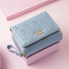 Light blue PU leather compact wallet with floral embroidery resting on a pink box.
