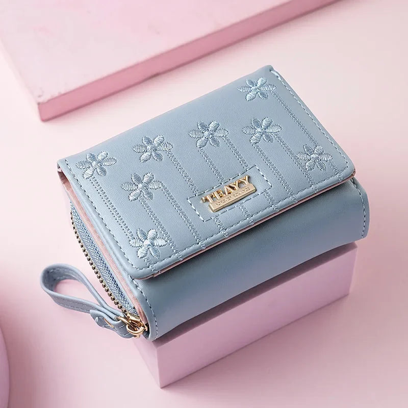 Light blue PU leather compact wallet with floral embroidery resting on a pink box.