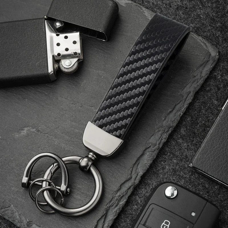 A close-up shot of a carbon fiber leather keychain attached to a dark surface.