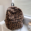 A brown leopard print plush backpack hanging in front of a white window blind.