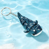 A dark blue devil ray figurine with a silver chain attached, floating in clear water.