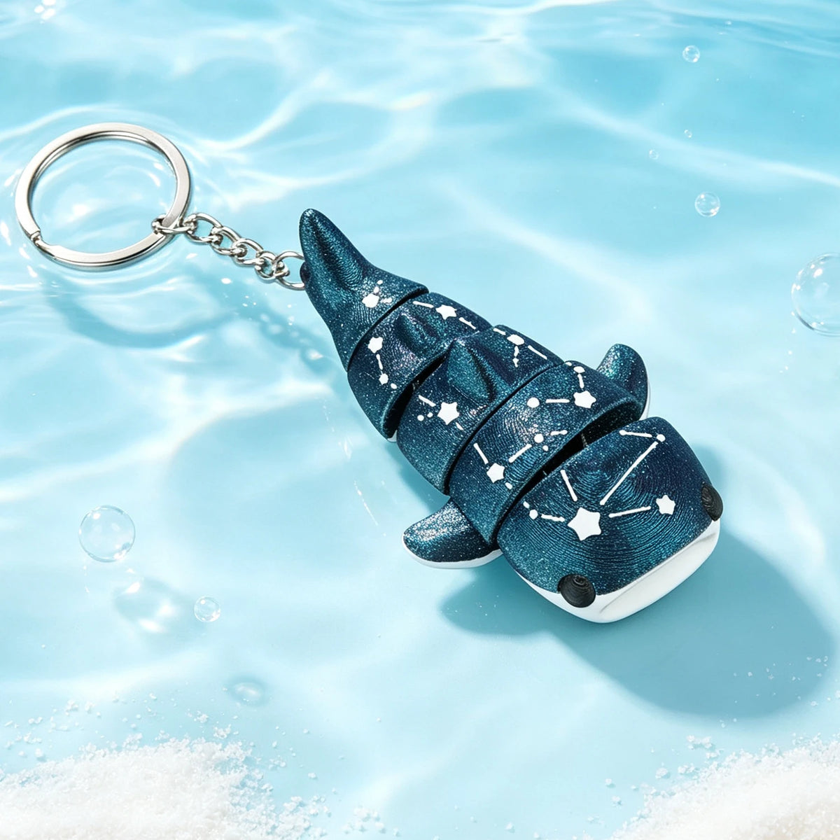 A dark blue devil ray figurine with a silver chain attached, floating in clear water.