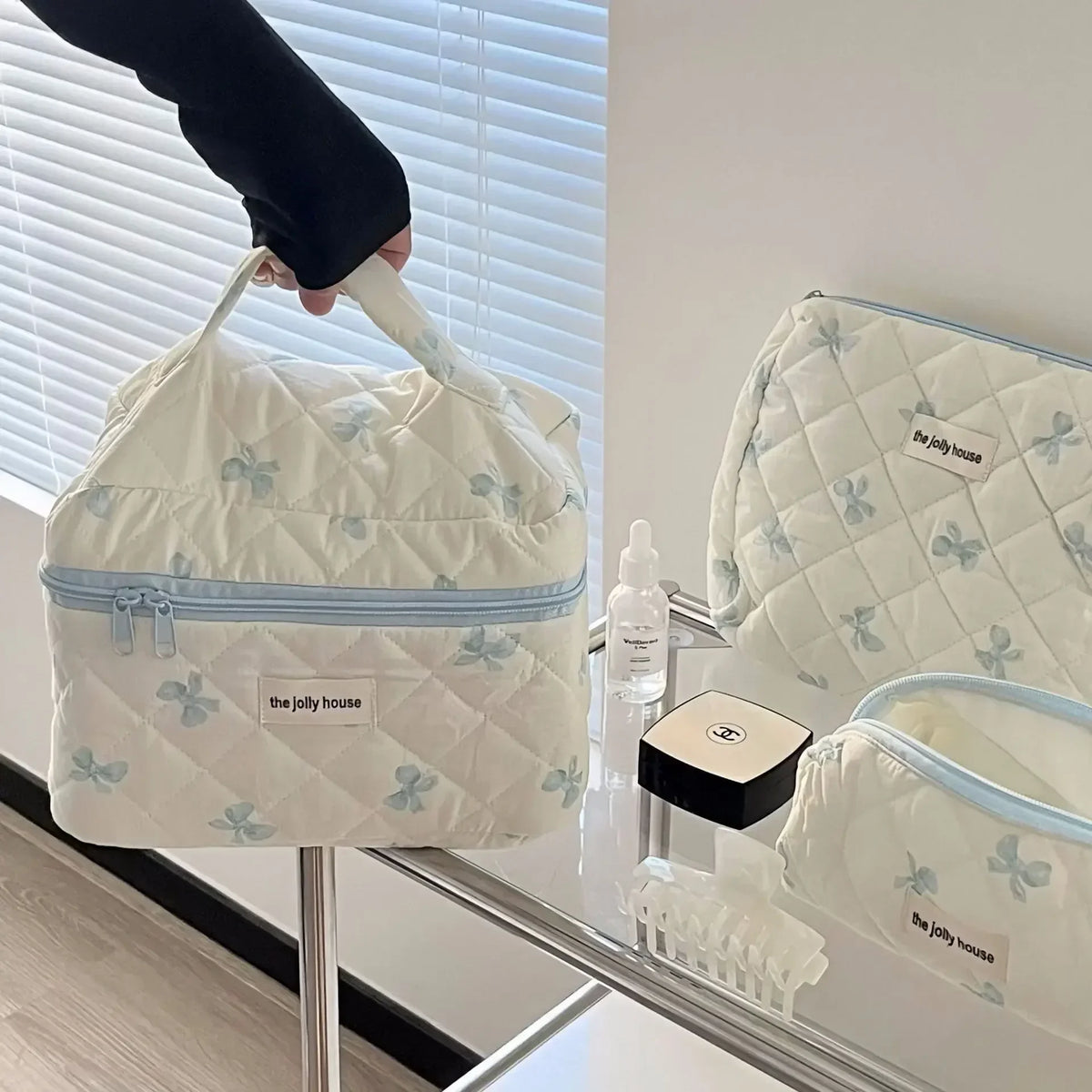 Sac de rangement cosmétique de couleur crème, à motif matelassé et accents bleu clair, exposé sur une étagère en verre.