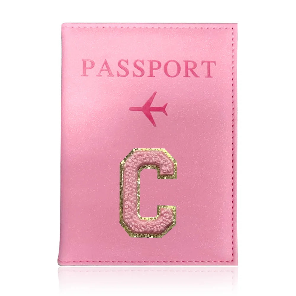 A pink leather passport holder with a gold initial C and a pink airplane symbol.