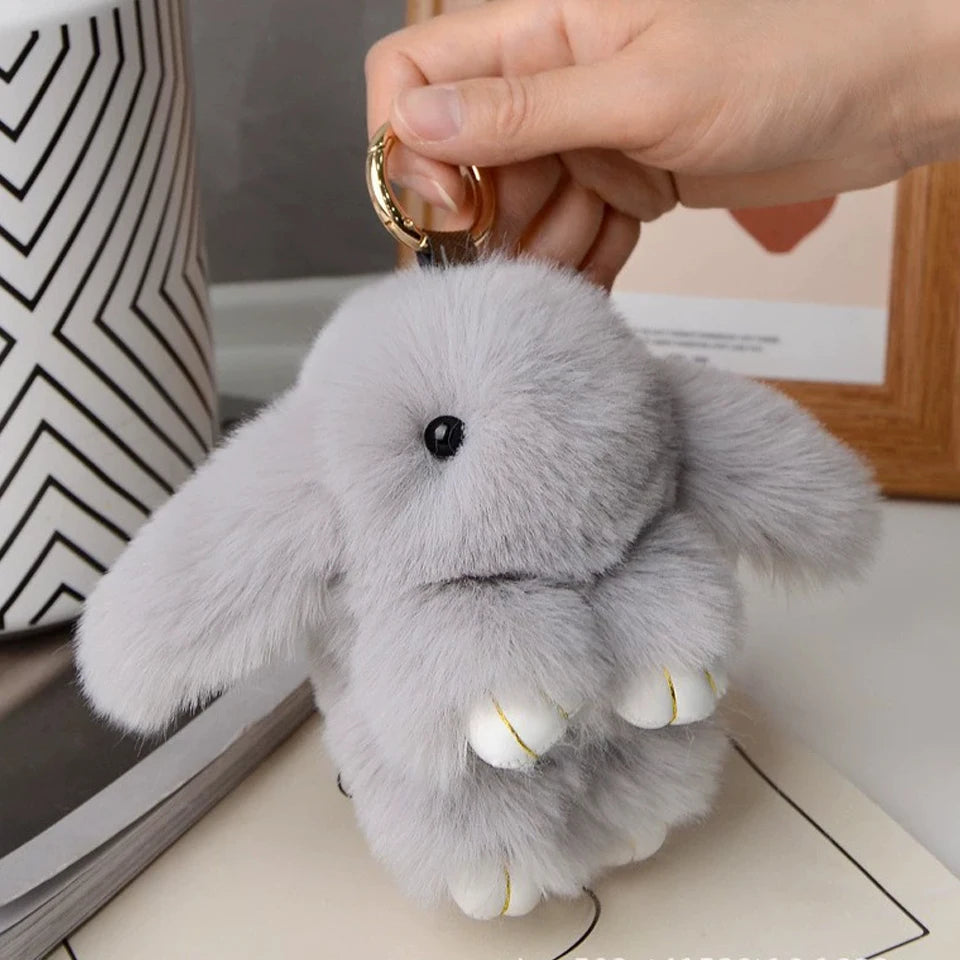 A soft gray plush rabbit with white accents is being held by a hand, shown against a light background.