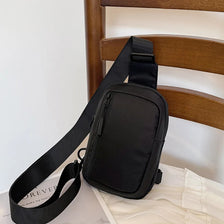Black versatile unisex chest bag hanging on a wooden bed frame.
