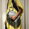 A hand holds a silver fringed clutch bag with black tassels against a yellow and black striped garment.