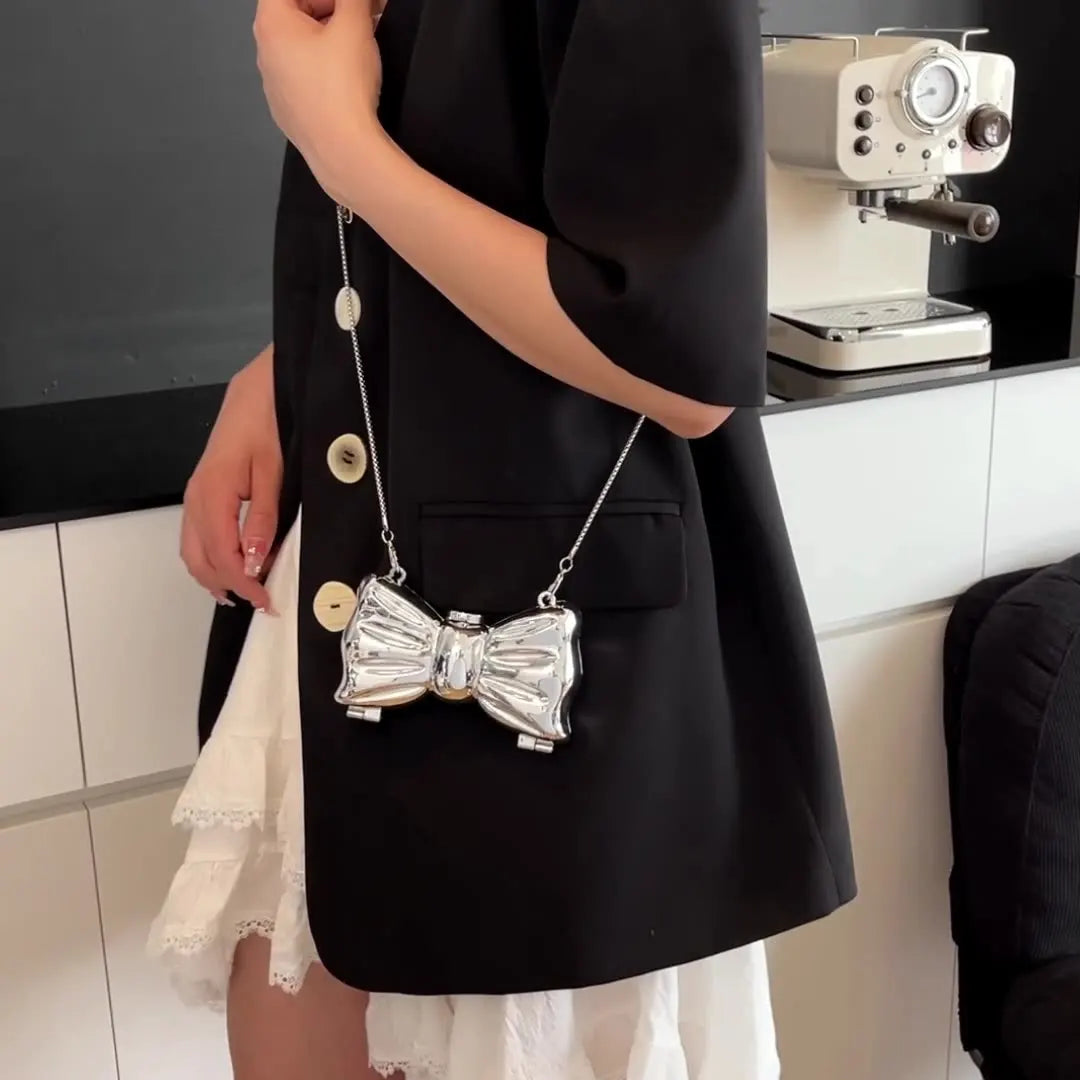 A woman holds a black blazer dress with white lace trim and a silver acrylic bow clasp mini handbag on a chain strap.
