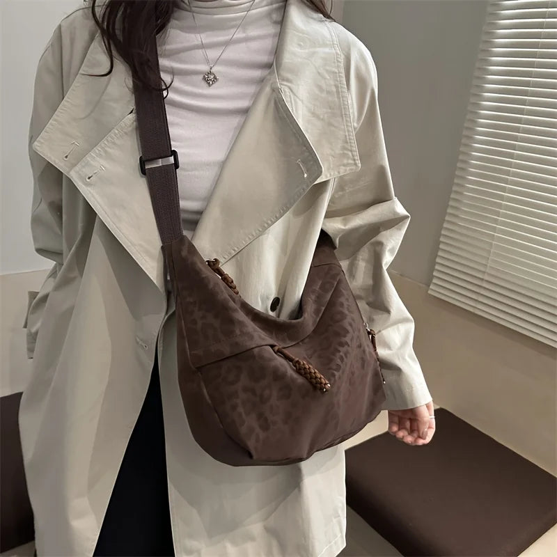 A person wearing a white trench coat holds a brown leopard print crossbody bag.