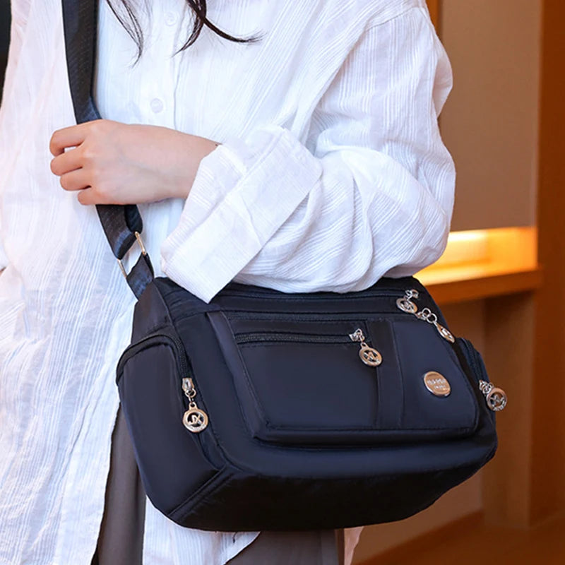 A woman wearing a white shirt carries a black waterproof nylon crossbody tote bag.