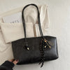 A black PU leather tote bag with gold hardware is displayed on a white surface next to a card.