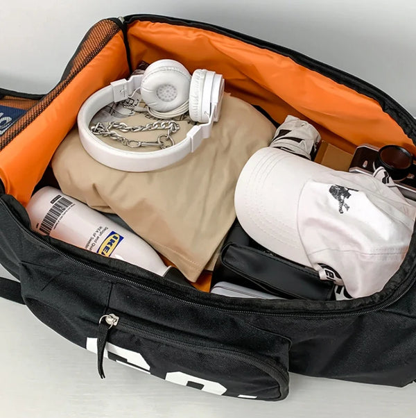 A black backpack is open, showing a tan lining and various items including headphones, a shirt, and a baseball cap.