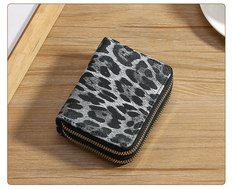 A black and gray leopard print double zipper wallet resting on a wooden surface.
