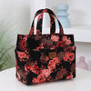 A black cloth tote bag with a floral pattern featuring pink and burgundy roses, resting on a white surface.