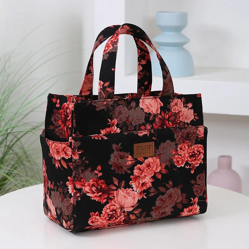 A black cloth tote bag with a floral pattern featuring pink and burgundy roses, resting on a white surface.